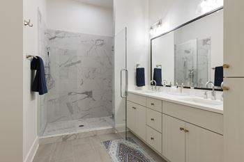 A bathroom with a marble shower and white cabinetry.